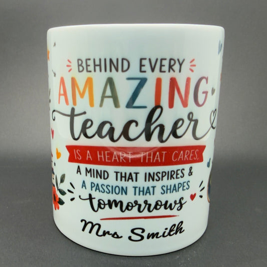 A white ceramic mug with a colorful printed quote that reads 'BEHIND EVERY AMAZING teacher IS A HEART THAT CARES.